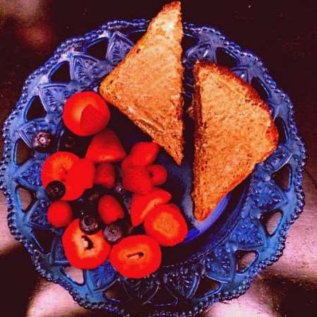 Pan tostado con mantequilla de cacahuate o almendra y fruta, principalmente fresas y moras azules.