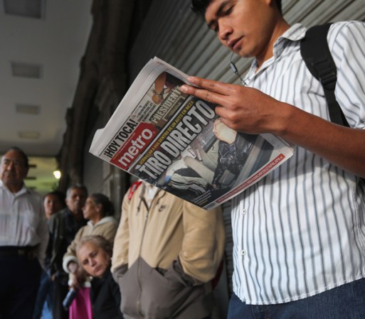 Un votante lee un periódico local con la portada relacionada a las muertes a causa del narcotráfico mientras espera que abran las casillas.