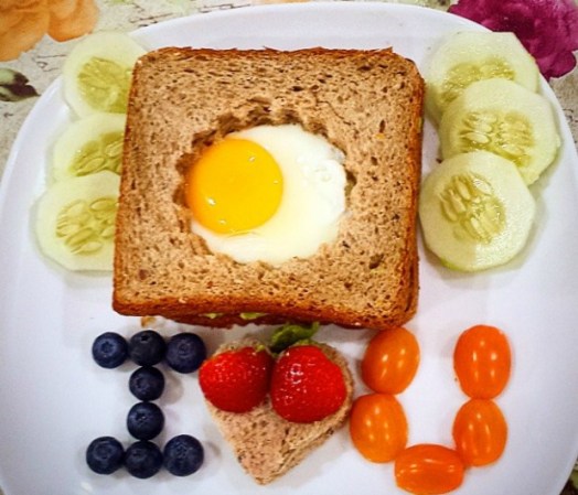Un amoroso desayuno: sándwich de huevo frito en un pan cortado, ensalada de pepino y moras diversas.
