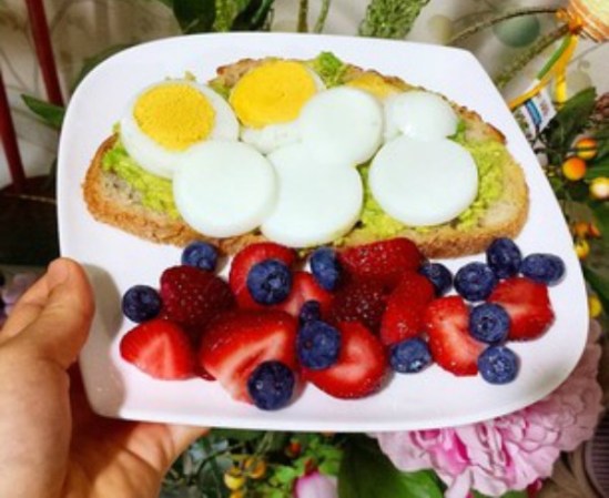 Sándwich de aguacate con rebanadas de huevo duro, acompañado por una porción generosa de frutillas.