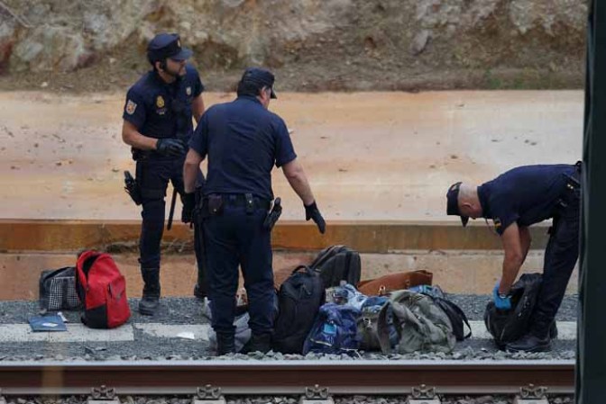 SANTIAGO DE COMPOSTELA, SPAIN - JULY 25: Police officers collect baggage at the scene of a train crash, which killed at least 77 people, on July 25, 2013 at Angrois near Santiago de Compostela, Spain. The crash occurred on Wednesday at 8.40pm as the train approached the north-western Spanish city of Santiago de Compostela, with 247 passengers on board. At least 77 people have died and a further 131 have been reported injured. The crash occurred on the eve of Santiago de Compostela's main religious festival, which has been cancelled by the City's officials. (Photo by Pablo Blazquez Dominguez/Getty Images)