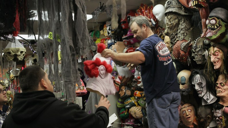 En Chicago, Illinois, un vendedor muestra una máscara de Halloween a un cliente, en la tienda Fantasy Costumes, que permanece abierta las 24 horas para satisfacer las necesidades de los compradores.