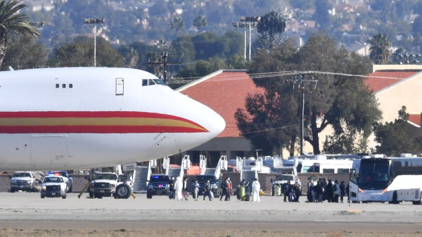 A team in white biohazard suits watch as some of the approximately 200 passengers walk to waiting buses upon arriving on a charter flight from Wuhan, China, after landing at March Air Reserve Base in Riverside, Calif. Wednesday morning Jan. 29, 2020. The flight originated from the area where the coronavirus outbreak started. All the passengers will be held in quarantine for an unknown duration.