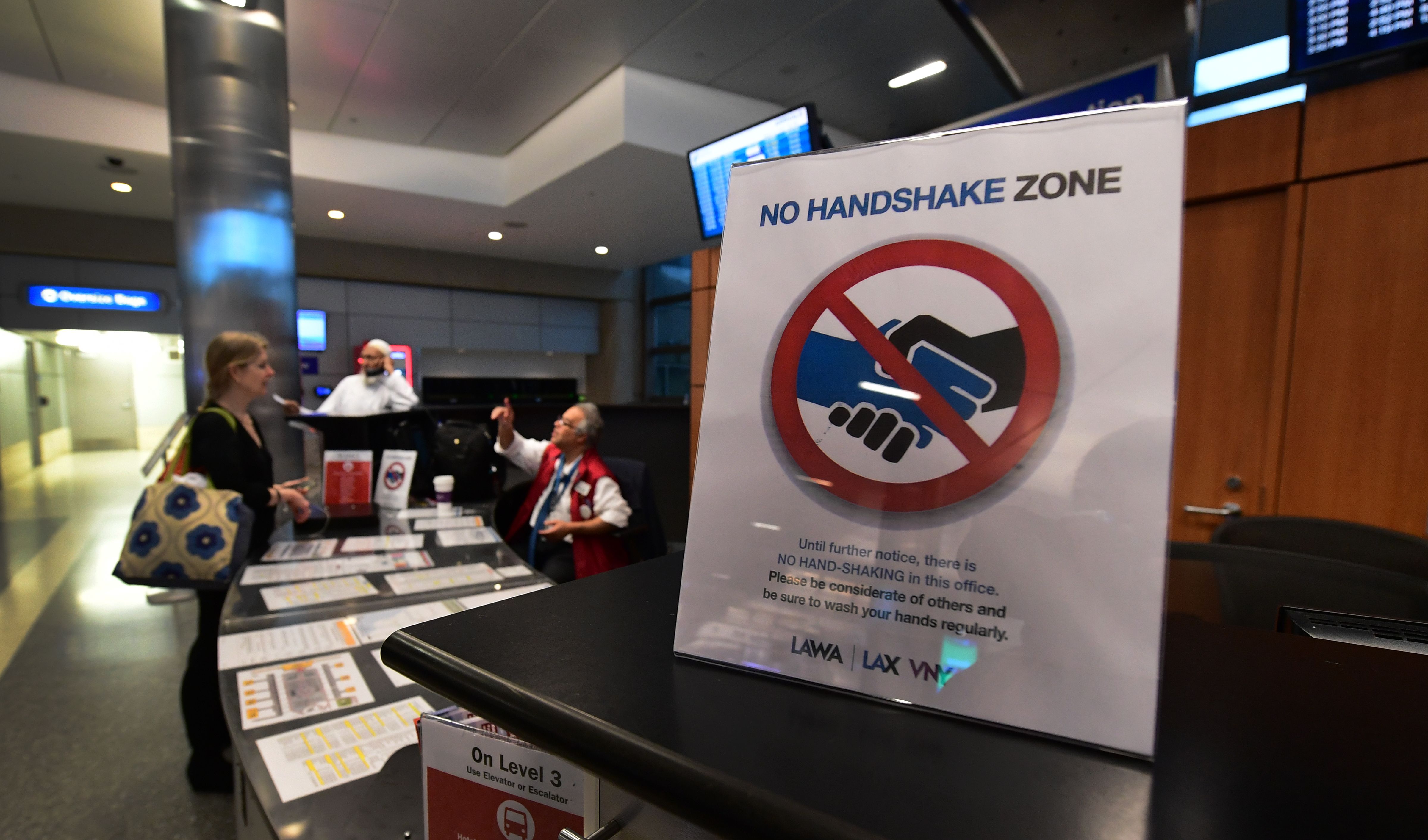 Un viajero pide información en un puesto al lado de un recordatorio de no estrechar la mano por las preocupaciones sobre el Coronavirus en el Aeropuerto Internacional de Los Ángeles (LAX) el 12 de marzo de 2020 un día antes de que una prohibición de viajar en Estados Unidos llegara a 26 países europeos en medio de las precauciones en curso sobre el Coronavirus. (Foto de Frederic J. BROWN / AFP) (Foto de FREDERIC J. BROWN / AFP a través de Getty Images)