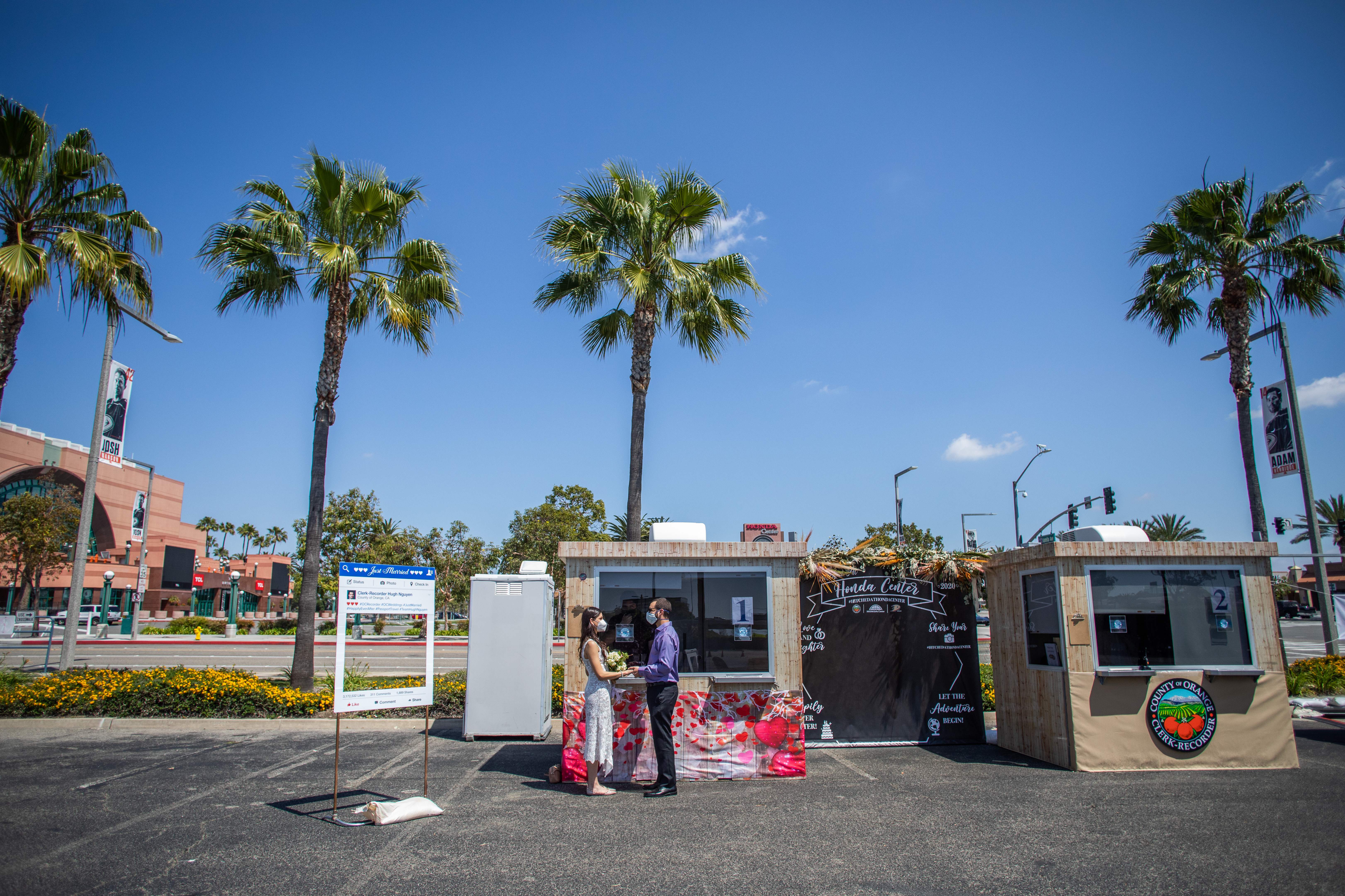 Un oficial une en matrimonio a Kev McCaryan (R) y su prometida Tiffany en el estacionamiento del Honda Center, el 21 de abril de 2020 en Anaheim, California. - Los empleados del Registro de Empleados del Condado de Orange implementaron una variedad de técnicas de distanciamiento social para emitir licencias de forma segura y casarse con parejas durante la nueva pandemia de coronavirus. (Foto de Apu GOMES / AFP) (Foto de APU GOMES / AFP a través de Getty Images)
