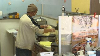 A man in a beanie stands over a griddle and flips a crepe