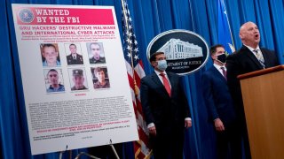 A poster showing six wanted Russian military intelligence officers is displayed on the left as officials to the right speak
