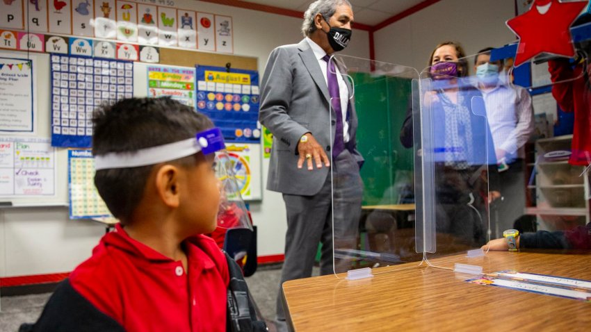 DISD Kindergartener looks up at teacher through clear mask and protective shield.