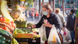 a woman selects vegetables outside a neighborhood grocery market