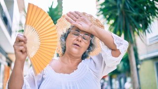 Middle,Age,Woman,With,Grey,Hair,Using,Handfan,On,A