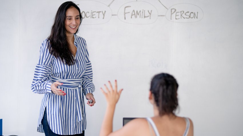 Rear view of female student sitting in the class and raising hand up to ask question during lecture