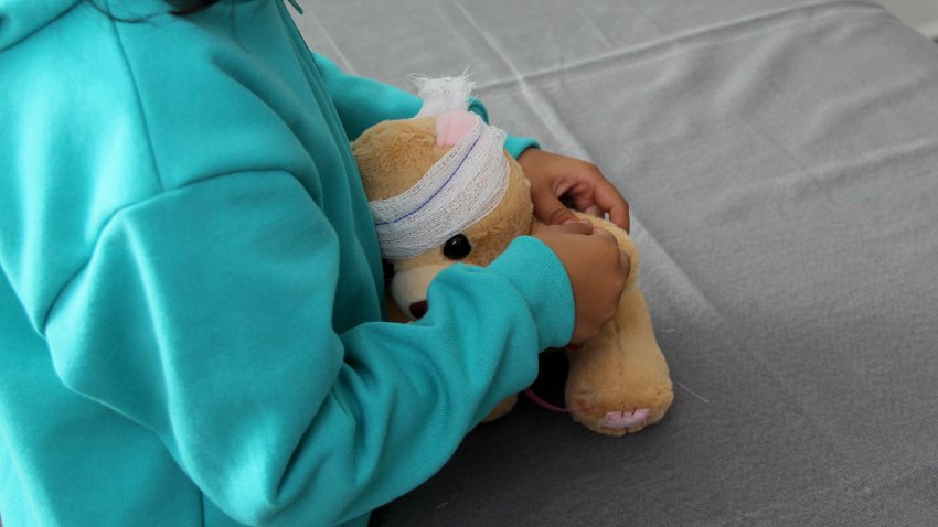 4-year-old brunette Latina girl with glasses represents mistreatment and physical abuse in her teddy bear with bandages on her head