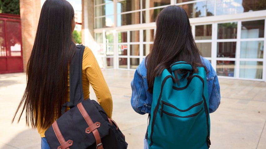 Two chinese students with backpacks stroll outside school, chatting and embodying youth and friendship. A vibrant campus scene captures the excitement of learning and growth